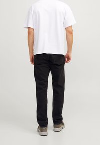 Camiseta blanca de manga corta y jeans negros, con un ajuste relajado. Los jeans tienen bolsillos traseros y se combinan con zapatillas deportivas grises.