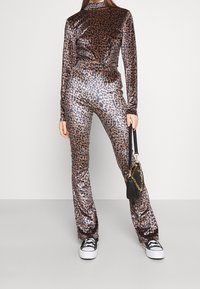 Completo due pezzi con stampa leopardata in tessuto lucido marrone. Top a maniche lunghe con collo alto e pantaloni a zampa. Abbinato a una piccola borsa nera.