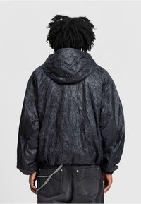 Schwarze, zerknitterte Stoffjacke mit Kapuze. Hat eine lockere Passform und elastische Bündchen. Auffällige Textur und schlichtes Design.