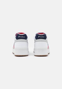 Pár bílých tenisek Polo s námořnickými modrými akcenty z pohledu ze zadní strany, s červenými interiéry a nápisem "Polo" na patkách.