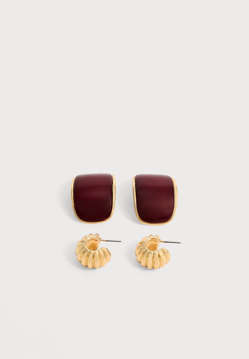 Deux paires de boucles d’oreilles : l’une avec des pierres rectangulaires rouge foncé incurvées entourées d’or, l’autre avec de petits anneaux dorés rainurés avec des tiges.