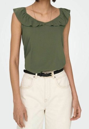 Mujer con blusa sin mangas verde oliva con escote con volantes, pantalones de tiro alto color blanco roto y cinturón negro con hebilla dorada.