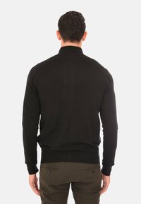 Vista posteriore di un maglione nero in maglina con colletto alto, polsini e orlo a coste, caratterizzato da una texture liscia e un design aderente.