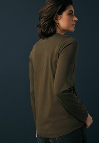 Olivengrünes Langarmshirt aus weichem Stoff, mit rundem Halsausschnitt und lockerer Passform, kombiniert mit dunkler Jeans.