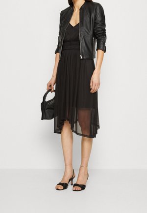 Veste bomber en cuir noir sur une robe noire avec un ourlet fluide et asymétrique. Portée avec des talons décolletés noirs et un petit sac à main.