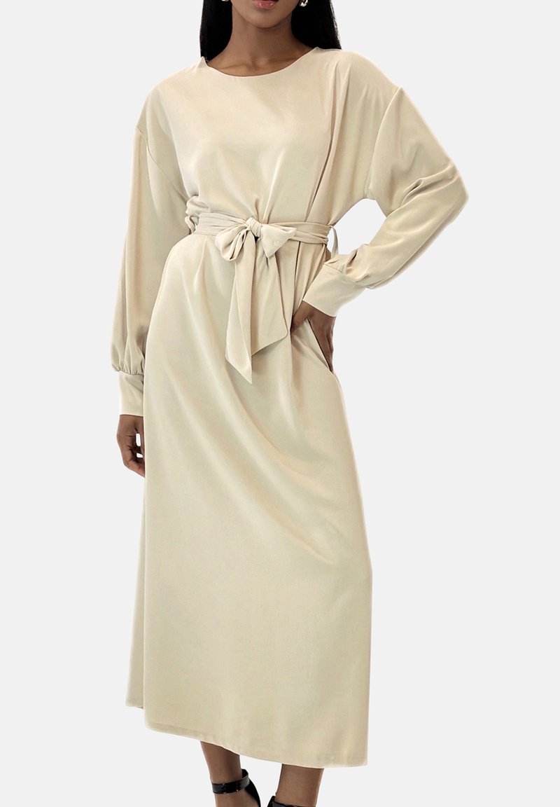 Robe midi en satin beige avec manches longues, encolure ronde et détail de taille nouée. Caractérisée par une texture lisse et une coupe décontractée.