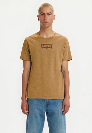 Brun bomulds T-shirt med rund hals og korte ærmer, prydet med et mørkebrun Levi's-logo på brystet. Bæres sammen med blå jeans.
