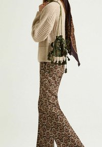 Pull beige tricoté à coupe décontractée, associé à un pantalon évasé marron à motifs avec des formes abstraites. Accentué par un sac vert à cordon.