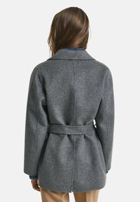 Grijze wollen jas met een ceintuur in de taille, ingesneden kraag en een recht gesneden ontwerp. De textuur lijkt iets fuzzy, geschikt voor koelere weersomstandigheden.