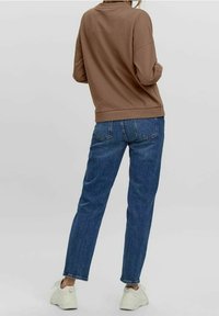 Hnědá mikina s přesazenými rameny, spárovaná s modrými zužujícími se džíny a bílými teniskami. Hladká textura, neformální design, minimální detaily.