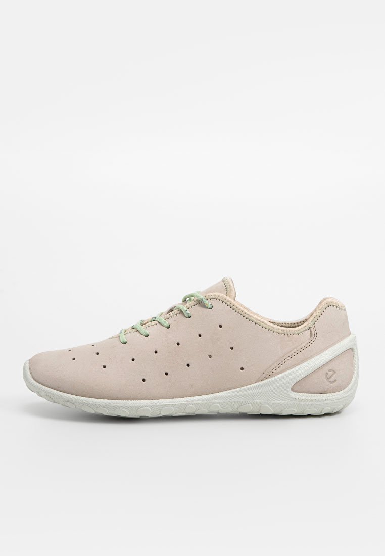 Jasnoróżowy but sportowy z perforowaną cholewką, zielonymi sznurowadłami, białą gumową podeszwą i zaokrąglonym kształtem. Posiada fakturowany akcent na pięcie.