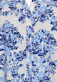 Un tissu à motifs bleu et crème présente des motifs floraux avec des détails complexes, une texture douce et une fermeture à boutons à l'avant.