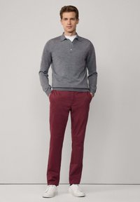 Grijze gebreide pullover met een kraag en drie knopen, gecombineerd met bordeauxrode chino's en witte sneakers. Eenvoudige, getailleerde silhouet en gladde textuur.
