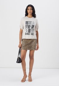Light gray short-sleeve shirt with leopard print and black text "DREAM" paired with a brown leopard print mini skirt and strappy sandals.