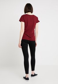 Burgundyröd t-shirt med åtsittande passform, korta ärmar, mjukt bomullsmaterial, kombinerad med svarta skinny jeans och svarta sneakers. Enkel, avslappnad design.