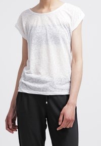 Vit, lätt T-shirt med uppvalda ärmar, som har ett subtilt strukturerat mönster och avslappnad passform, ihop med svarta byxor.