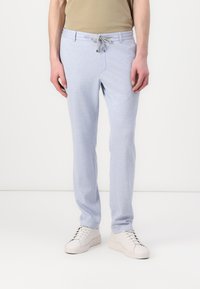 Pantaloni de trening bleu deschis cu talie ajustabilă, textură netedă și croială îngustă. Purtați cu adidași albi și o cămașă bej.