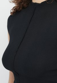 Κοντινό μιας γυναίκας που φοράει εφαρμοστό μαύρο αμάνικο τοπ με ριμπ ύφανση και λεπτομέρεια κεντρικής ραφής.