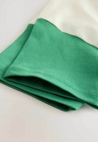 Katoenen T-shirt met een crèmekleurig bovenste gedeelte en een effen groene onderkant. De stof is zacht met een geribbelde textuur aan de randen.