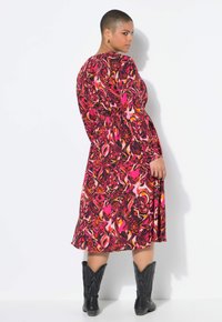 Langärmliges Kleid mit Blumenmuster in verschiedenen Schattierungen von Pink, Rot und Schwarz; mit taillierter Taille; kombiniert mit schwarzen Cowboy-Stiefeln; fließender Stoff.