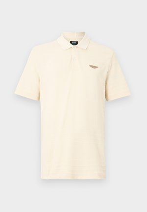 Lys beige polotrøye laget av mykt stoff, med en tredelt knappeliste og en liten teksturert logo på venstre bryst.