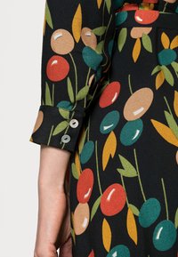 Černý dlouhý rukáv s vícebarevnými abstraktními oválnými a listovými vzory a dvěma malými bílými knoflíky na manžetě.