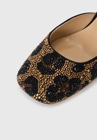 Beaded slip-on shoe featuring a black and gold leopard pattern, with a smooth interior and textured exterior made of assorted gemstones.