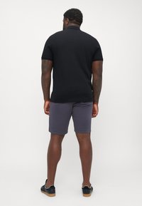 Cămașă polo neagră cu mâneci scurte, asortată cu pantaloni scurți gri, purtată cu adidași negri cu talpă din cauciuc. Material neted cu un design ajustat.