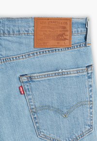 Light blue denim jeans featuring a brown leather label with embossed text, orange stitching, and a small red Levi's tag on the back pocket.