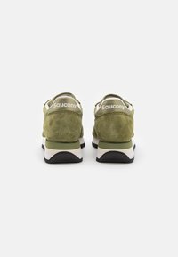 Grüne Wildleder-Sportschuhe mit einem weißen Logo auf der Ferse, ausgestattet mit einer klobigen weißen und schwarzen Sohle und einem schlichten, geschwungenen Design.