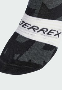 Calcetín con patrón en negro y gris que presenta una banda blanca con el texto "TERREX"; fabricado en tejidos texturizados, con un ajuste estructurado y puntera reforzada.