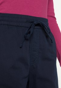 Pantalons de jogging navy avec une taille élastique et un cordon de serrage. Tissu lisse avec des poches latérales. Associés à un haut rose texturé.