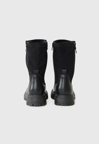 Bottines noires à talons avec une base en cuir lisse et une tige en textile, dotées de fermetures éclair latérales, présentées sur un fond blanc uni.