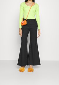 Neongrön randig långärmad topp, svarta utsvängda byxor, orange axelväska och fluffiga orangea sandaler.