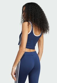 Námornícky crop top s bielym lemovaním a bočnými pruhmi, skombinovaný s námorníckymi legínami s vertikálnymi bielymi pruhmi. Hladká tkanina a priliehavý strih.