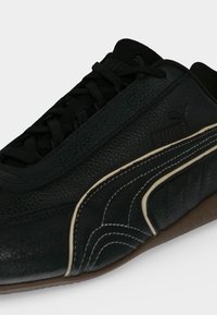 Μαύρο δερμάτινο αθλητικό παπούτσι Puma με μπεζ και άσπρη καμπυλωτή ρίγα και μαύρα κορδόνια που ταιριάζουν σε καφέ σόλα.