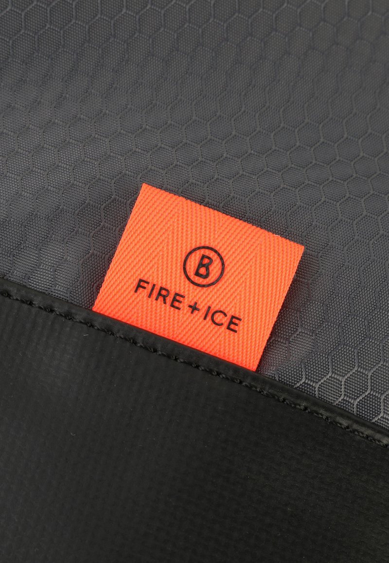 Schwarzer, strukturiertes Gewebe mit einem sechseckigen Muster, das ein oranges Etikett mit der Aufschrift "FIRE+ICE" und einem Logo zeigt. Dünne schwarze Nähte.