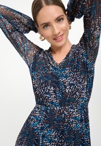 Langarmige jurk van doorzichtig marineblauw stof met een bloemenpatroon en accenten in blauw, wit en bruin. Gerimpelde halslijn en een getailleerde taille.