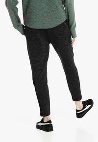 Black athletic joggers made of textured fabric, featuring a slim fit and contrasting side panels. Paired with black sneakers.