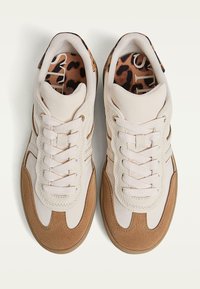 Para beżowo-brązowych zamszowych sneakersów z białymi sznurówkami i wkładkami w lamparta, widziana z góry na białym tle.
