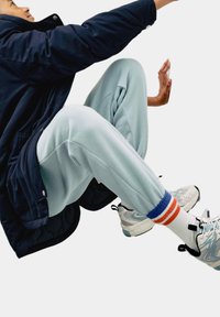 Svetle modré tepláky v kombinaci s tmavě modrou prošívanou bundou. Obsahují barevné pruhované ponožky (bílé, oranžové, modré) a šedé sportovní boty.