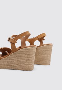 Sandalias de cuña en tono beige con tacón de yute texturizado y trenzado. Correa ajustable en el tobillo con diseño recortado. Forro interior suave y suela resistente.