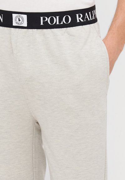 Jasnoszare dresy z bawełny z czarnym pasem, na którym widnieje napis "POLO RALPH LAUREN" w białym kolorze. Materiał jest miękki w dotyku i ma strukturalne wykończenie.