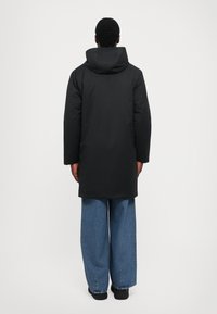 Parka nera con cappuccio, maniche lunghe e taglio dritto, abbinata a jeans in denim blu a vestibilità ampia. Design minimalista e senza motivi visibili.