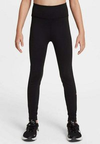 Leggings de sport noirs avec une taille haute, en tissu extensible et d'une coupe ajustée. Portés avec des baskets noires avec des accents blancs et gris.