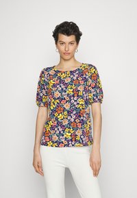 Top floral de mangas curtas com fundo azul-marinho, apresentando flores amarelas, cor-de-rosa e brancas. Decote redondo e mangas ligeiramente franzidas.
