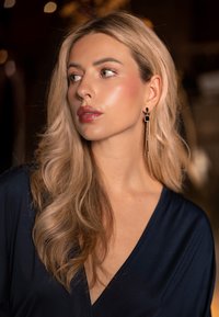 Boucles d'oreilles dorées avec un accent noir carré et des chaînes cascades. Le mannequin porte un vêtement bleu marine profond avec des cheveux blonds doux et ondulés.