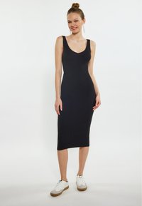Abito midi nero a costine con un design aderente, scollatura a V profonda e spalline regolabili, abbinato a sneaker bianche con dettagli grigi.