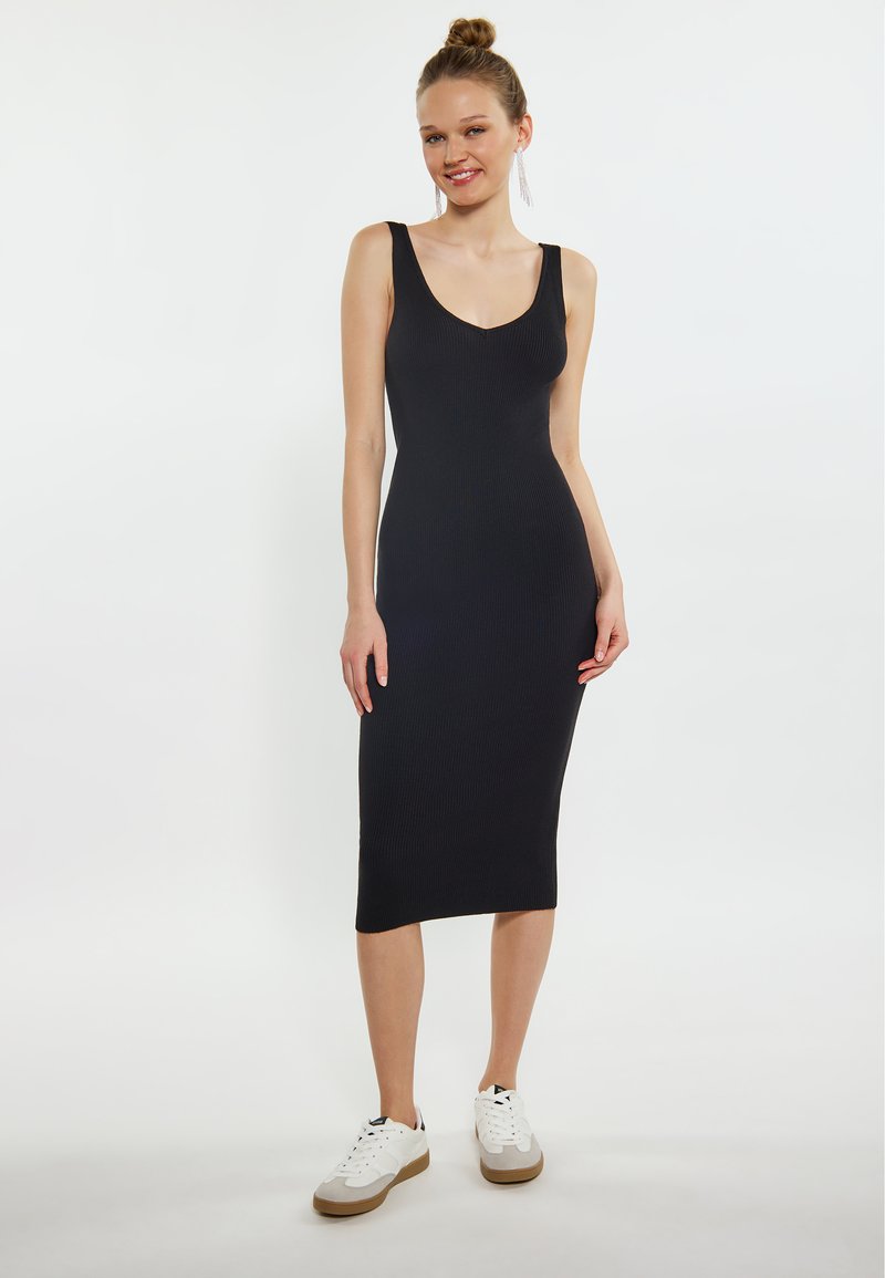 Abito midi nero a costine con un design aderente, scollatura a V profonda e spalline regolabili, abbinato a sneaker bianche con dettagli grigi.