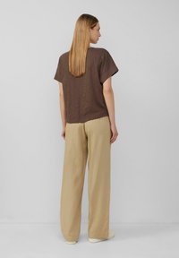 Bruin T-shirt met korte mouwen gecombineerd met losse, lichtbeige broek. Ontspannen pasvorm, zachte textuur en een eenvoudig ontwerp zonder zichtbare patronen of accenten.